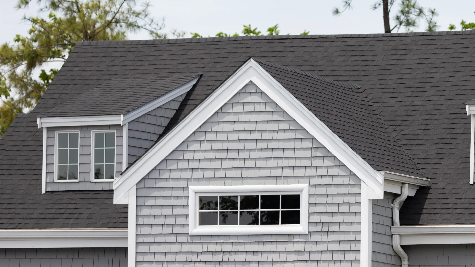 Close-up view of newly installed asphalt shingle roofing on home with white siding