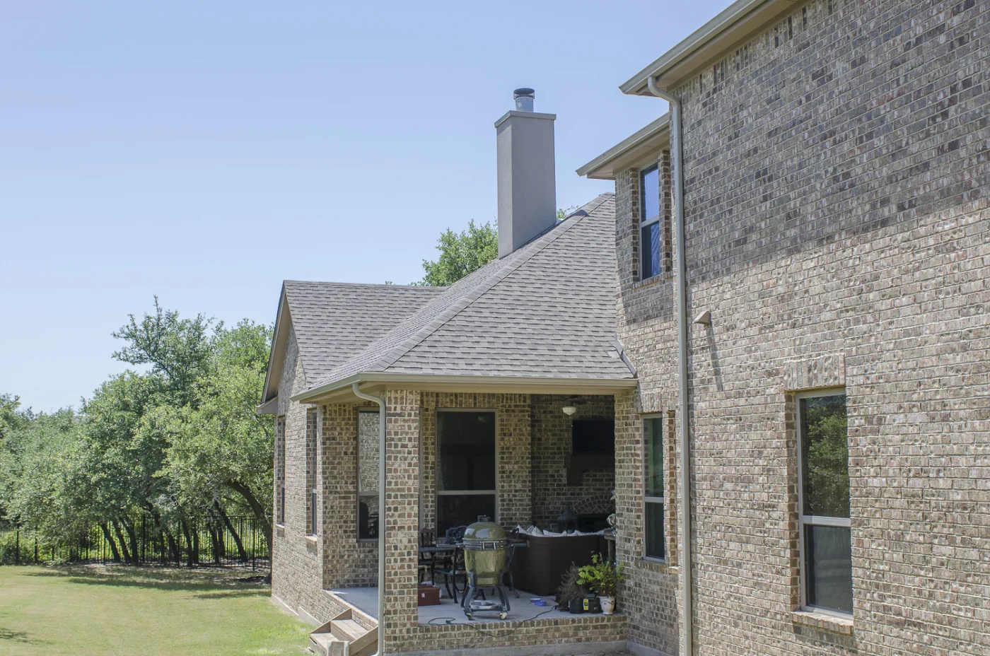 Great residential shingle Roof Replacements In Austin, TX | Freetail Roofing A two-story brick house with an asphalt shingle roof, a back patio, and a chimney on top.