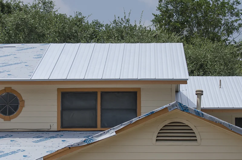 Tremendous Residential Roof Replacements In Austin, TX | Freetail Roofing A tan house with part of a metal roof installed and the rest ready for installation.
