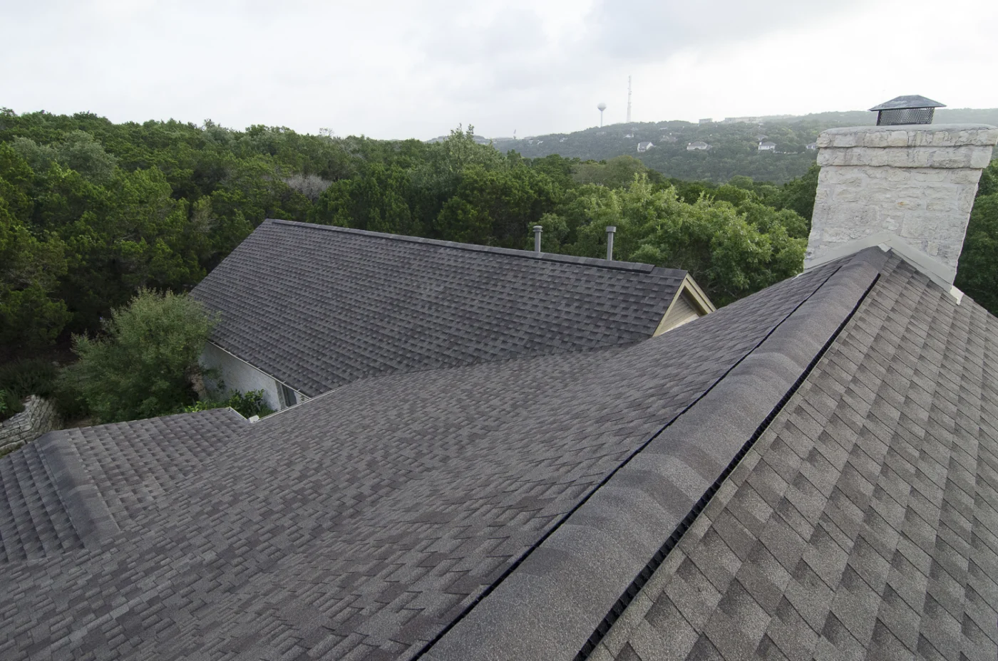 Tremendous Residential Shingle Roof Replacements In Austin, TX | Freetail Roofing A close-up view of an asphalt shingle roof with trees in the background.