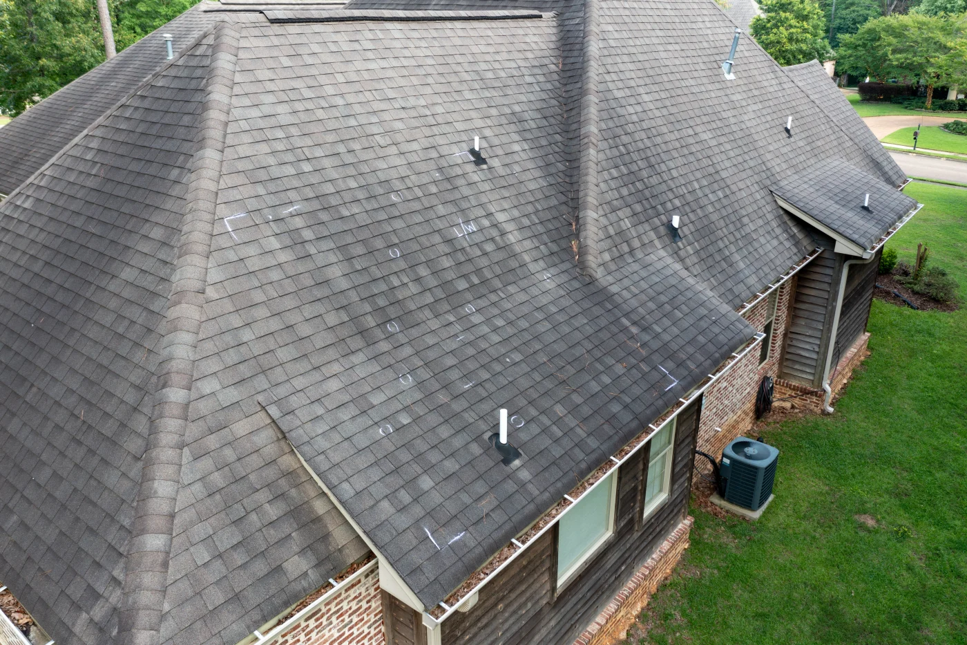 Close view of a shingle roof on a suburban home with damage spots indicated