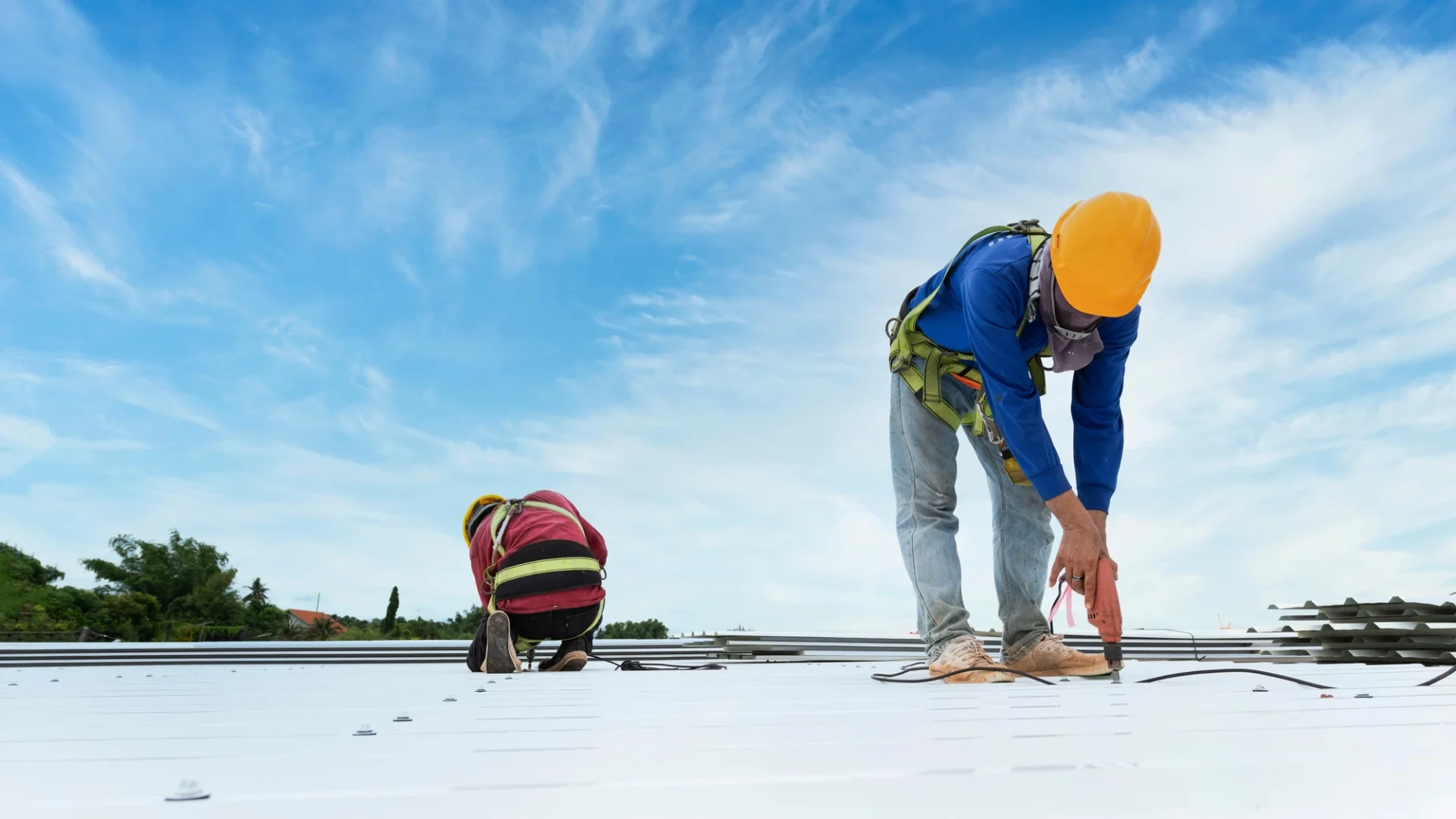 Low-angled view of two roofers installing a metal roof on a commercial building