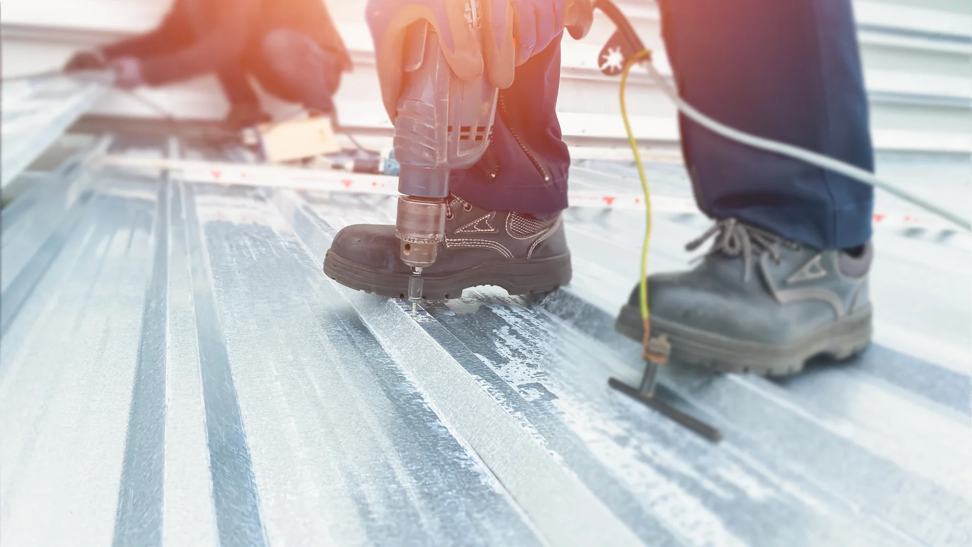 Close view of a roofing installing a panel in a metal commercial roof with a second worker visible in the background