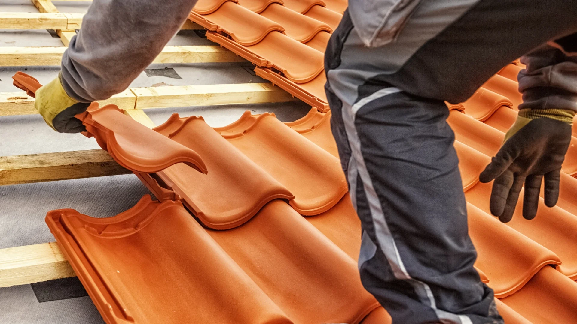 Close view of a roofer placing clay tiles during a roof replacement