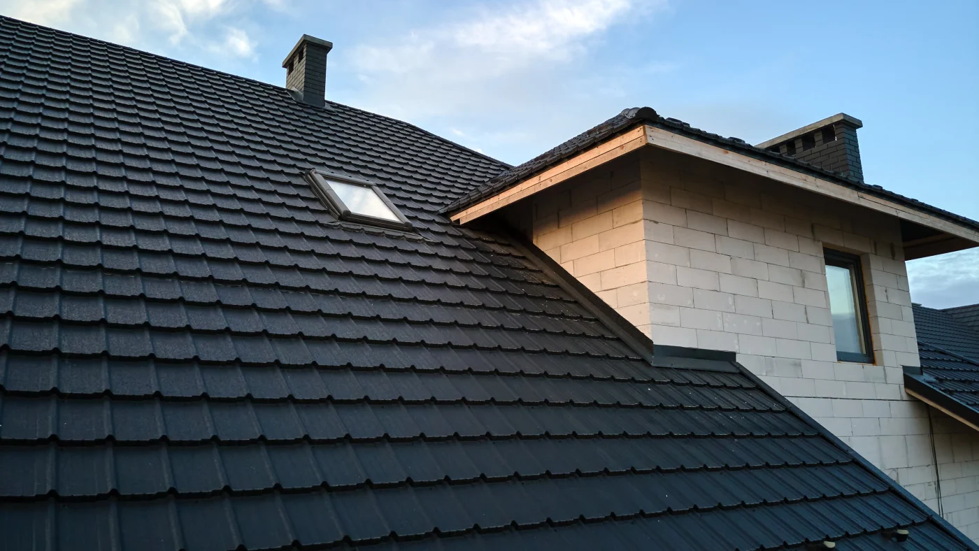 Close-up view of black tile roof with a chimney and attic windows