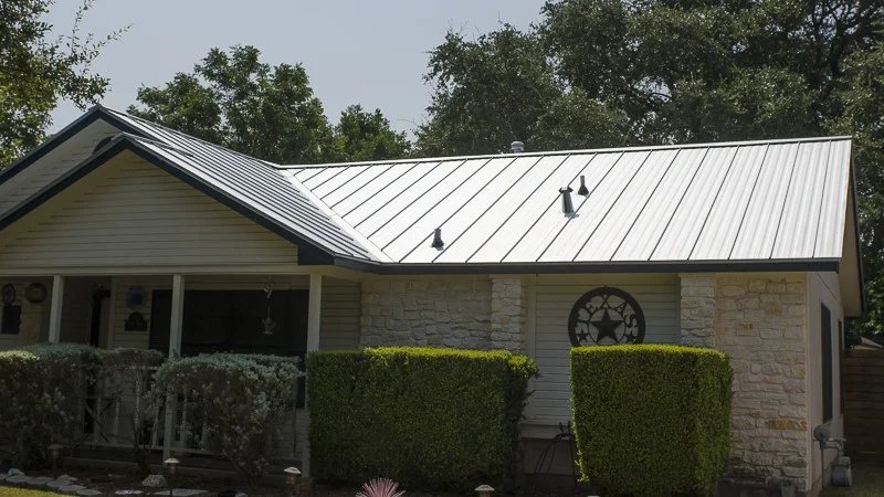 Texas home with black standing seam metal roof, hedges, bushes, and white porch