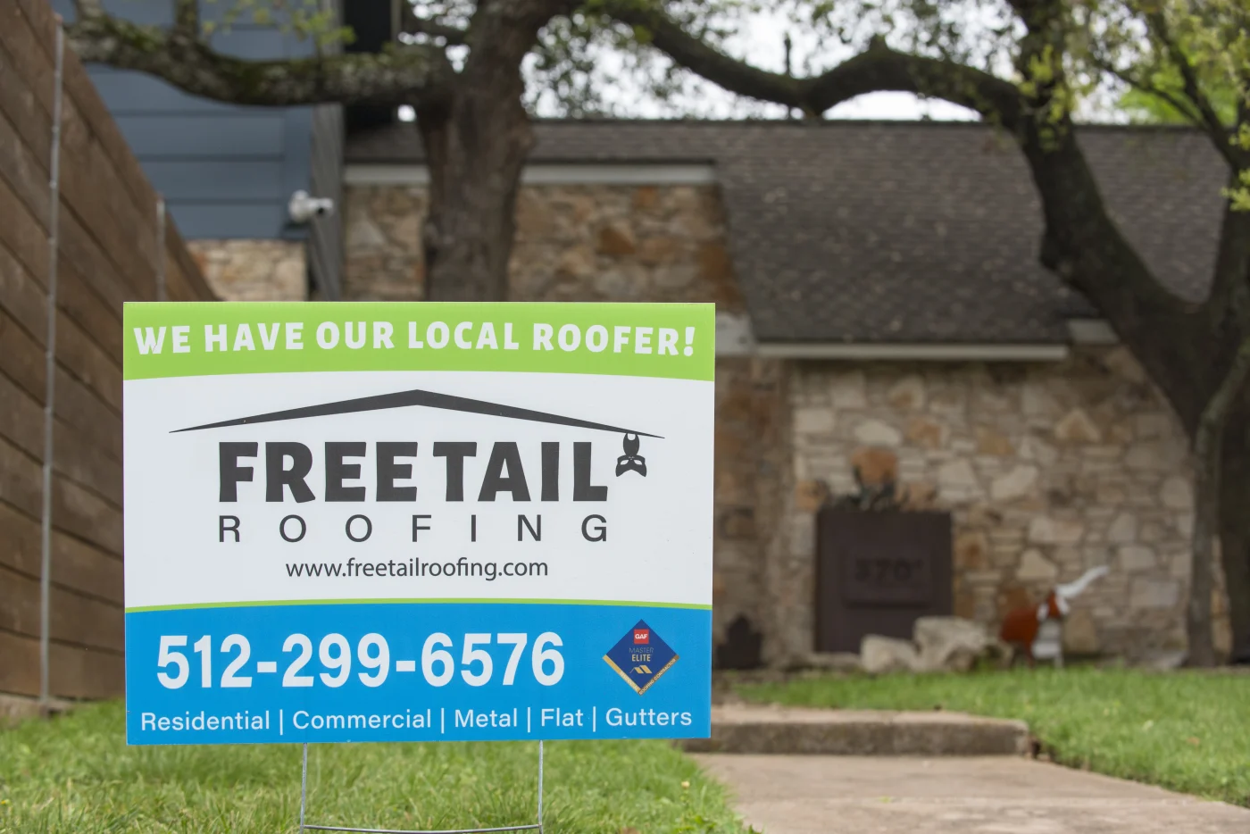 Image of a Freetail Roofing sign in front of a brick house with a newly installed roof in Burnet, TX