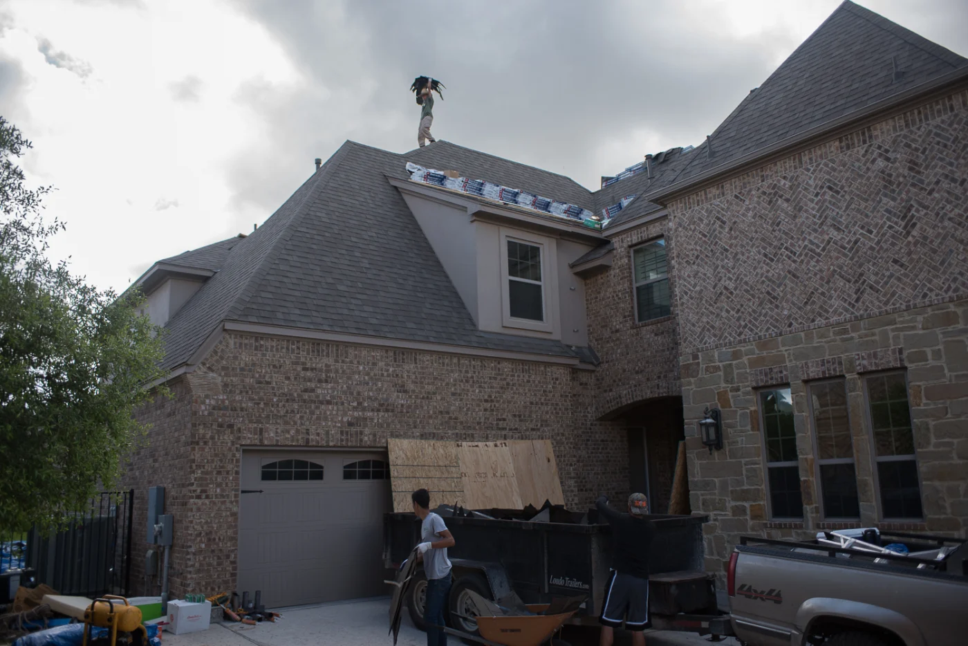 Roofers replacing an asphalt shingle roof on a two-story brick house.