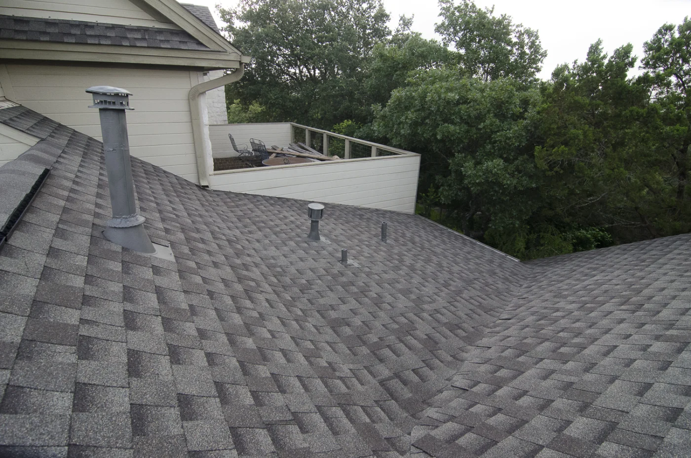 A close-up view of a new asphalt shingle roof on a tan house.