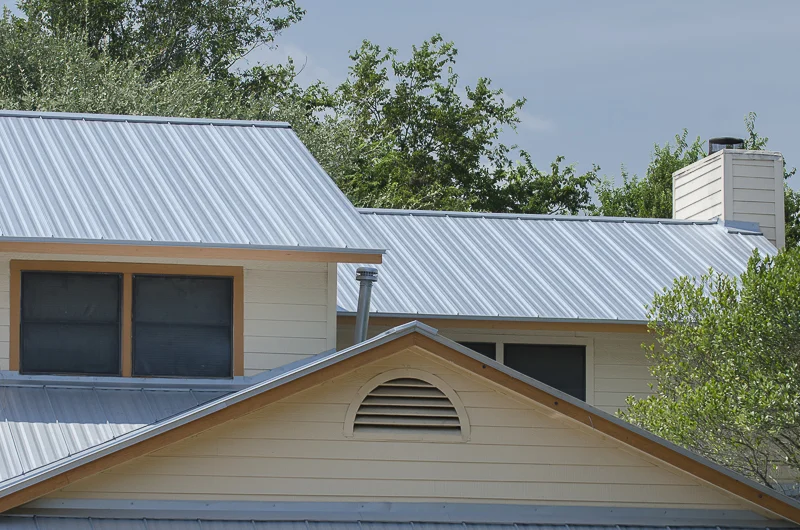 A close-up of the top of a tan house with a metal roof.