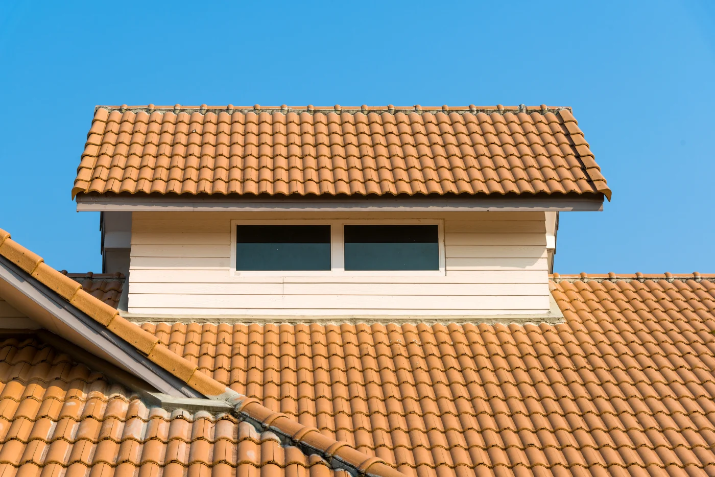 A close-up view of a tile roof on a tan two-story house.