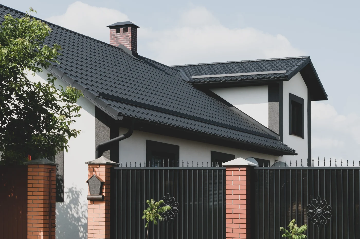 Superb Tile Residential Roof Replacements | Austin, TX | Freetail Roofing A beautiful house with a gated fence, white stucco siding, and rich, black tile roofing.